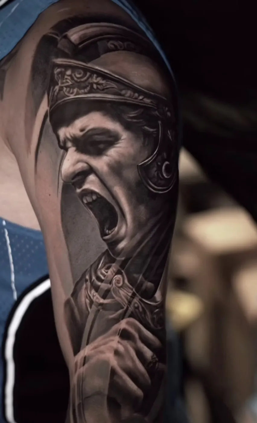 Black and grey tattoo of a screaming Roman centurion on the upper arm