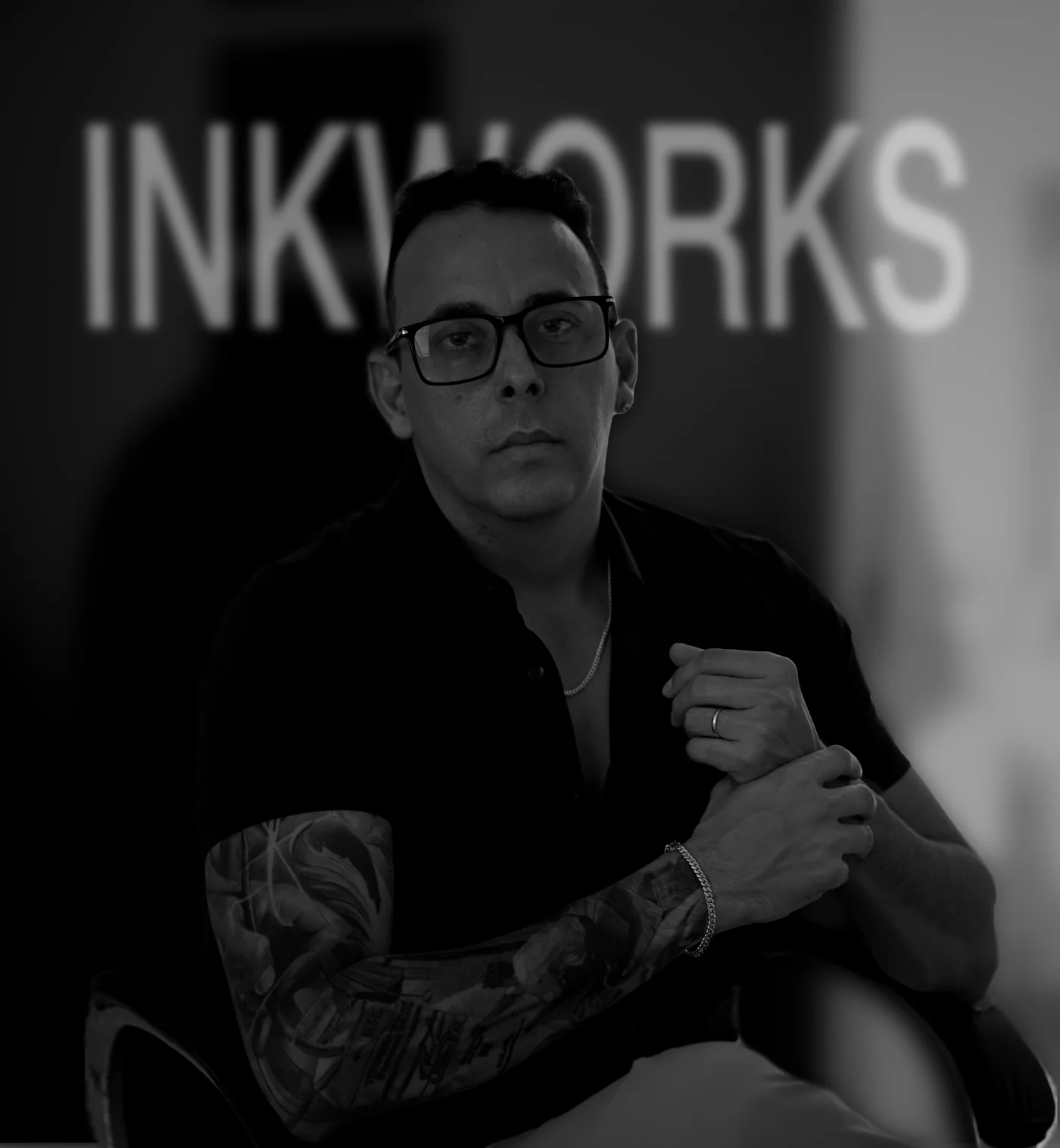 Black and white portrait of Harold Garcia seated in front of the InkWorks sign